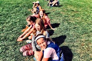 Girls, some in athletic attire, sitting on a field